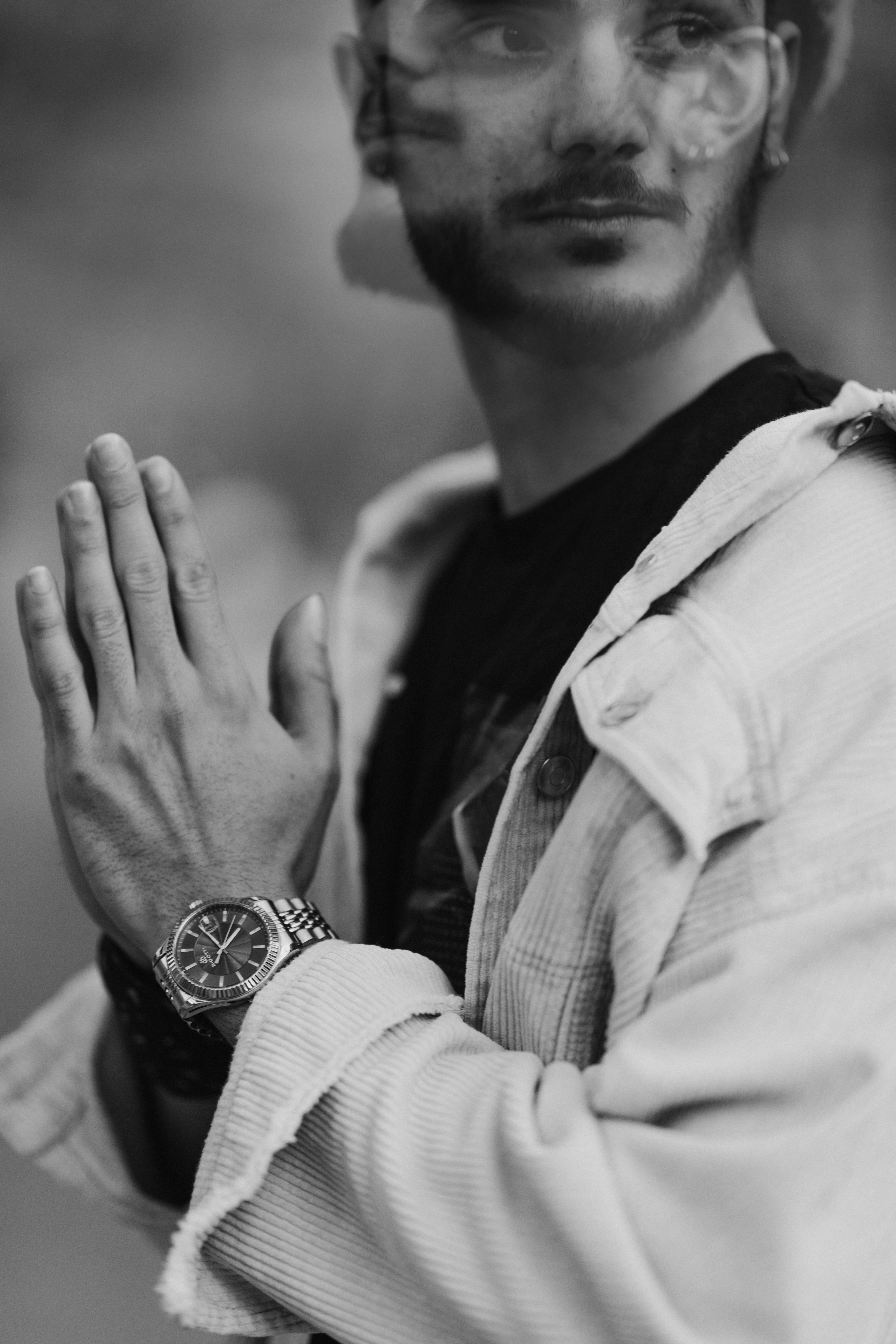 A fashionable man poses with hands together in a grayscale photograph, showcasing style and contemplation.