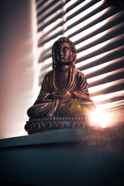 Free A serene Buddha statue is illuminated by a sunbeam through window blinds, creating a spiritual ambiance. Stock Photo