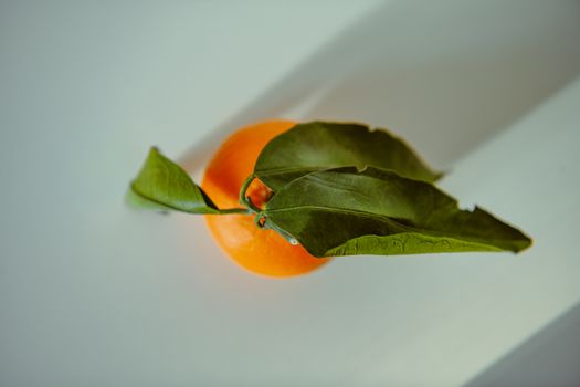 A fresh ripe orange with green leaves on a light background, captured in a minimalistic style.