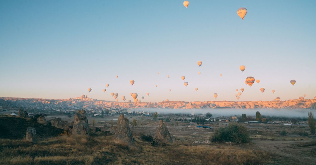 Scenic vista of numerous hot air balloons soaring above a rugged landscape during sunrise.