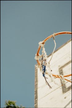 Old basketball hoop with frayed net under a clear blue sky, captured from below.