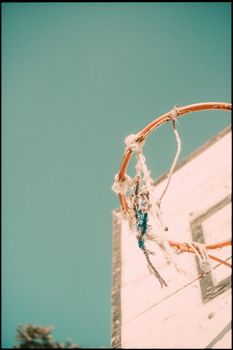 An old basketball hoop with a torn net set against a clear blue sky, captured from a low angle.