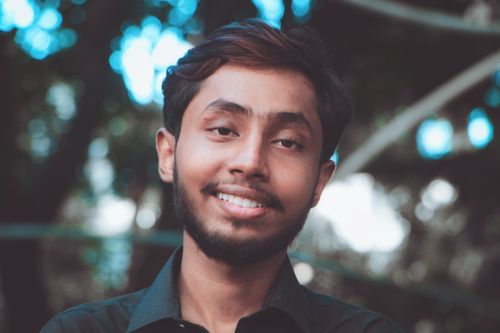 Free Close-up portrait of a smiling young man with a beard, set against an outdoor background. Stock Photo
