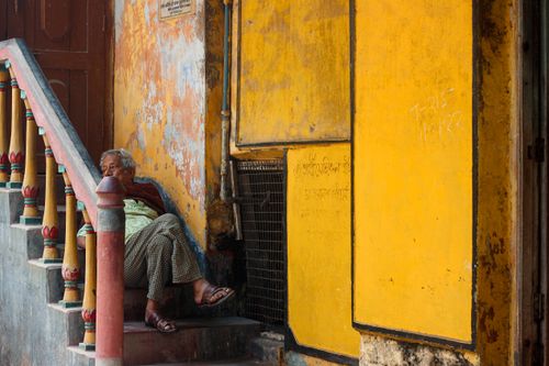 Free A senior woman relaxes on a colorful staircase next to a vivid yellow wall in an urban setting. Stock Photo