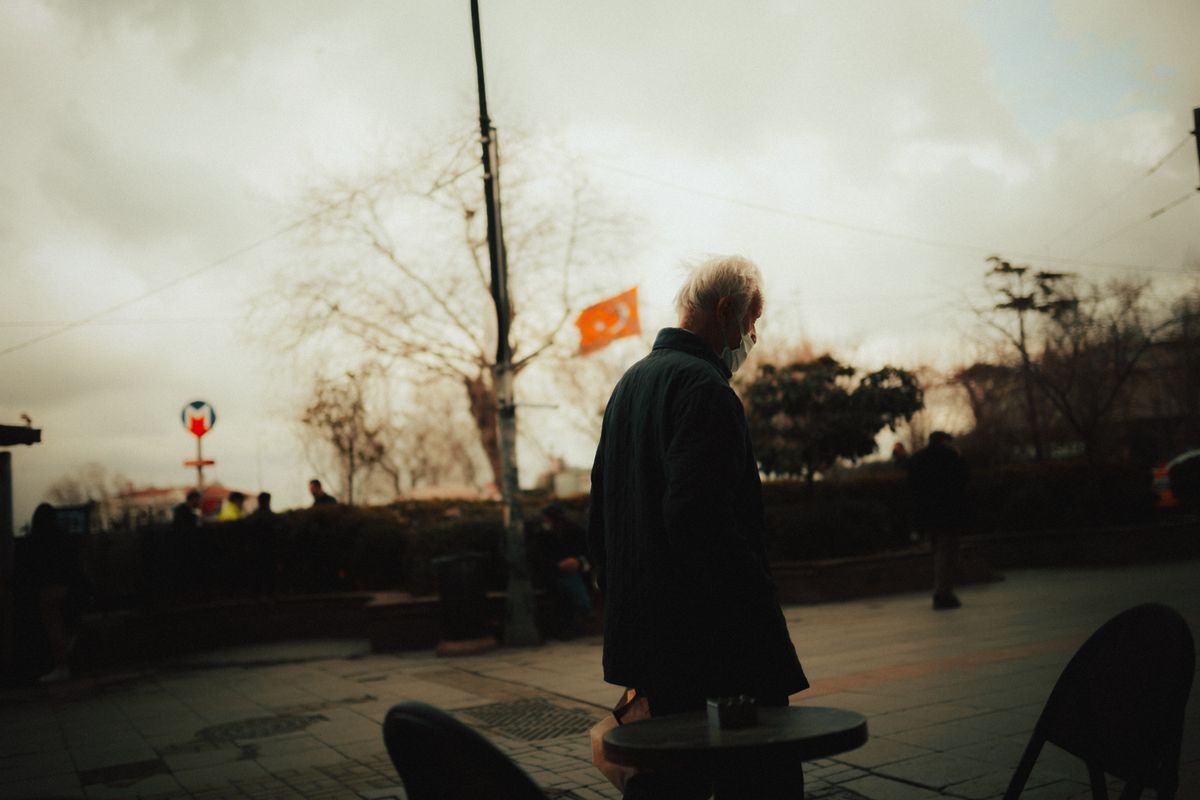 Sokakta yaşlı bir adam, arkasında bir bayrak
