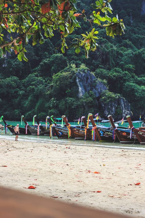 Free Scenic view of moored long-tail boats on a tropical beach with lush background. Stock Photo