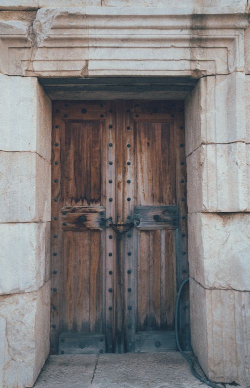Free A rustic wooden door with metal studs set in a stone wall, exuding vintage charm. Stock Photo