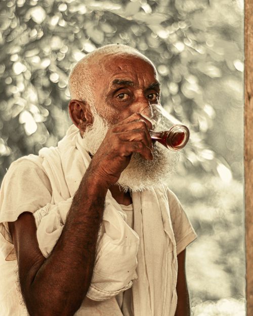 Free A senior man with a beard enjoying a drink from a glass mug, outdoors in natural light. Stock Photo