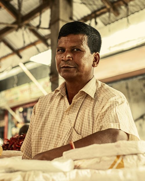 Free Casual portrait of a man smiling, seated at a market stall with rustic surroundings. Stock Photo