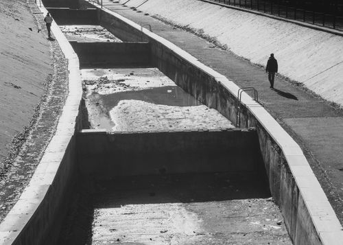 Free Black and white image of two people walking along an urban canal's concrete pathway. Stock Photo