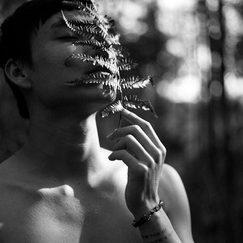 Grayscale Photo of a Topless Man Holding a Fern Leaf