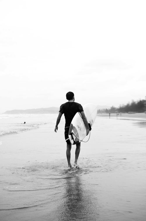 Free Black and white image of a lone surfer walking on a misty beach with a surfboard. Stock Photo