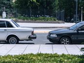 Two vintage cars parked on a sunny urban street amidst greenery and sidewalks.
