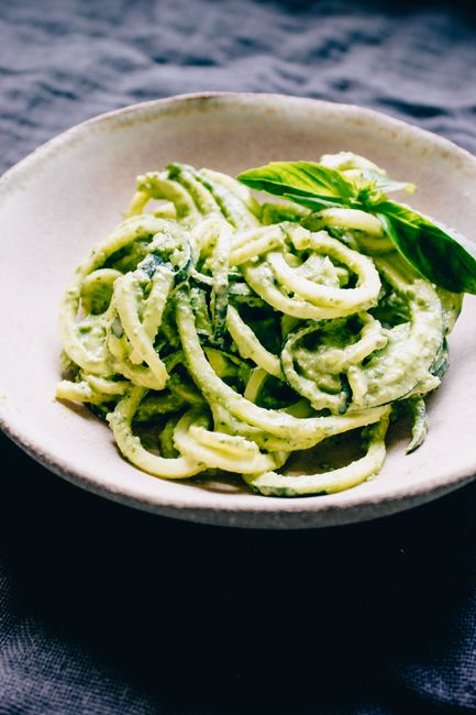A tangle of curly zucchini noodles spiralized into thin strands piled on a wooden board beside a handheld spiralizer tool.