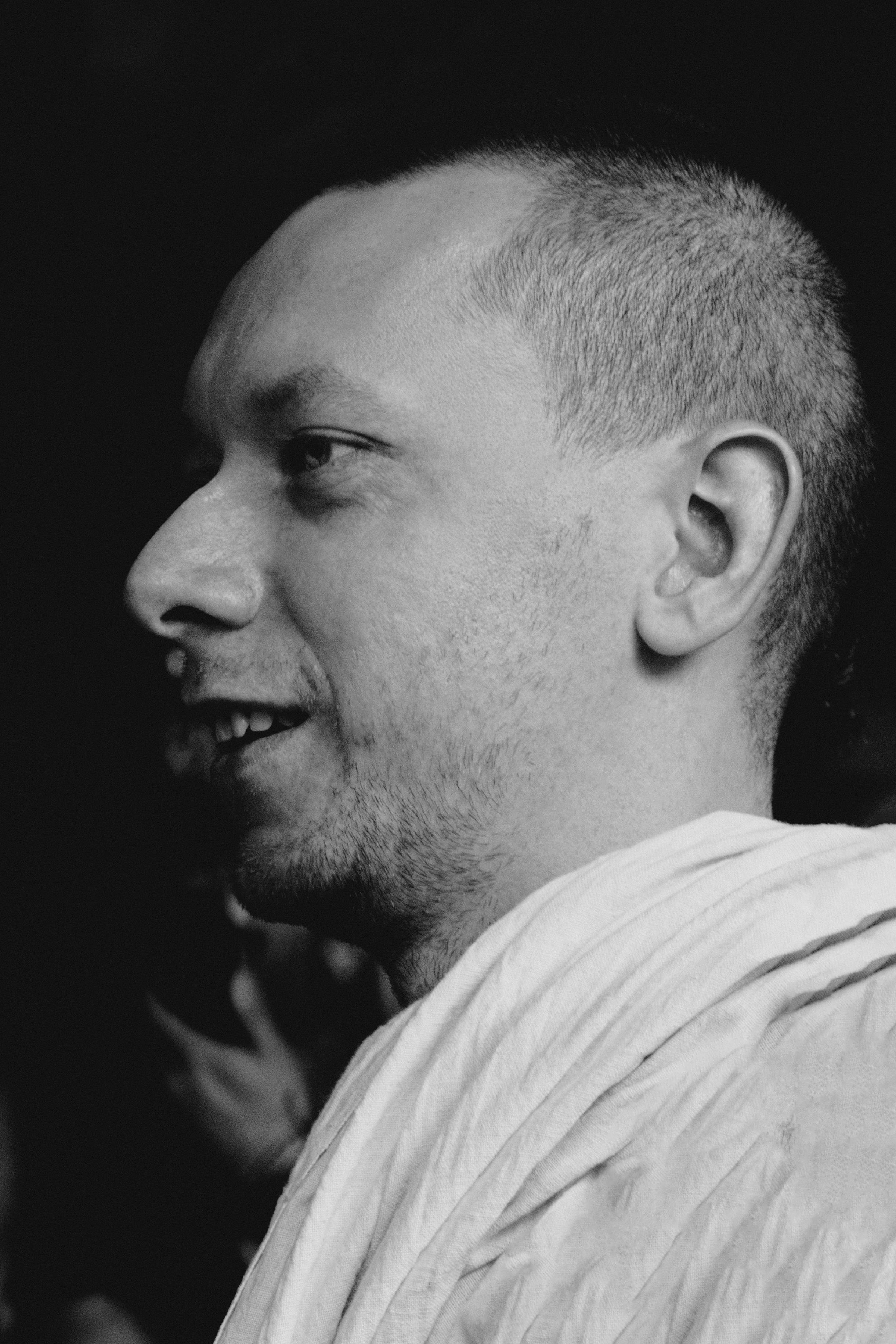 Striking black and white portrait of a smiling man with short hair against a dark background.