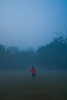 Silhouette of a young soccer player jogging on a foggy field in the early morning.