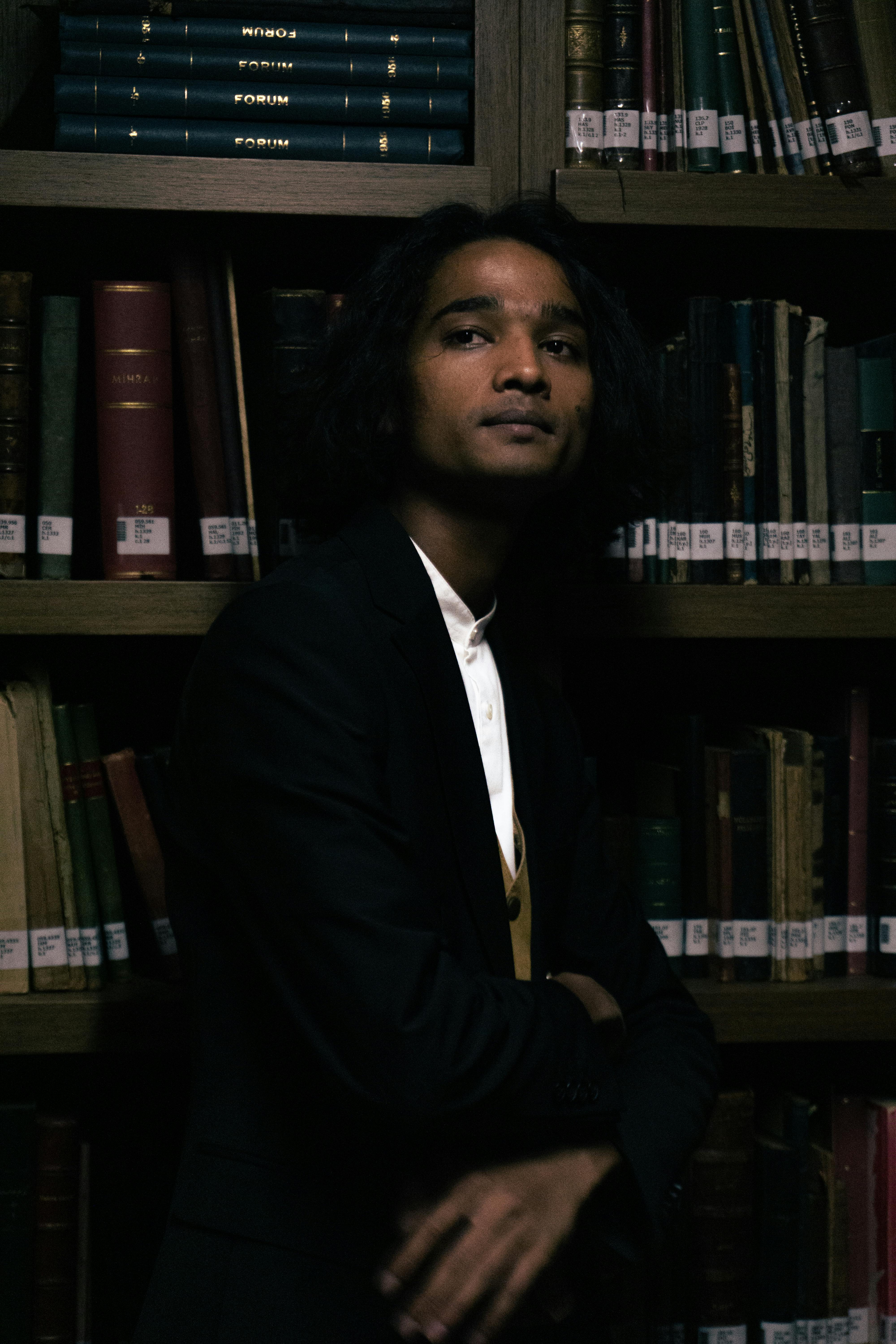 A contemplative man poses elegantly among classic library bookshelves.
