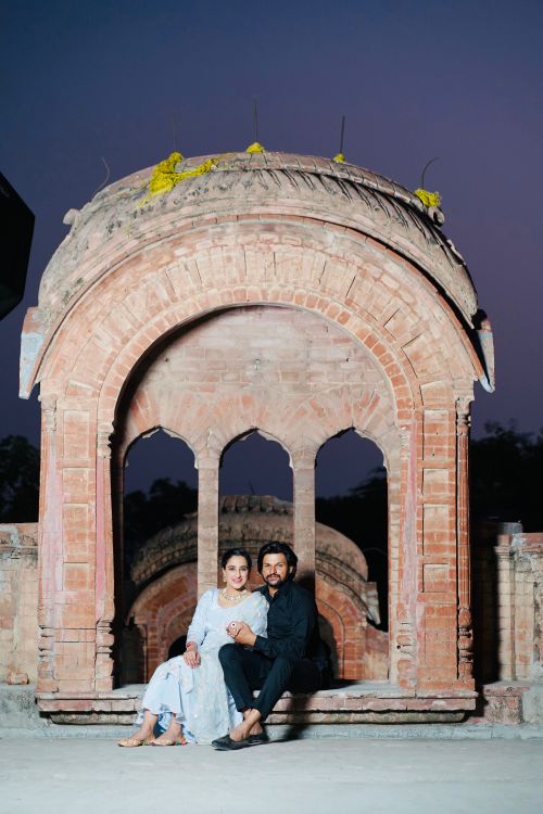 Free A couple sitting under a historic archway in Nabha, India at dusk, exuding romance and heritage. Stock Photo