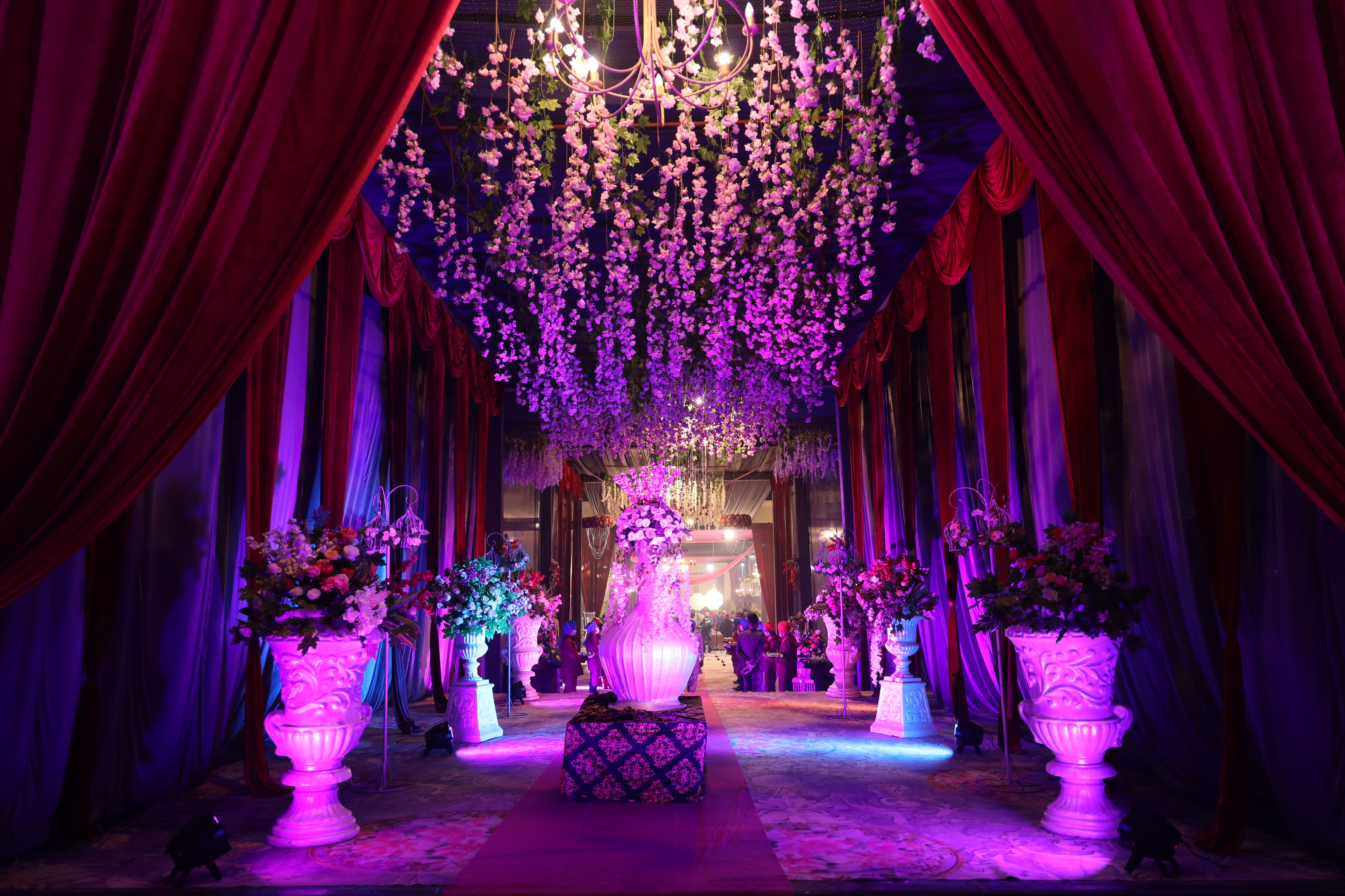 Elegant hallway with chandeliers, floral arrangements, and purple lighting creating a luxurious ambiance.