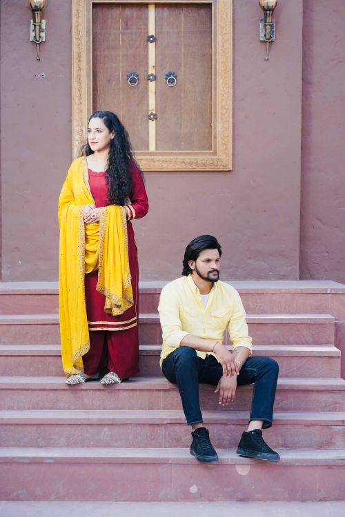 Free Man and woman in traditional attire sitting on steps outside a historic building. Stock Photo
