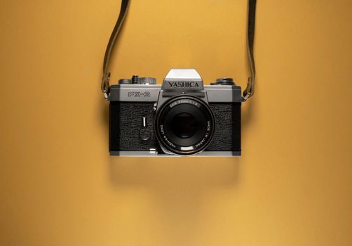 A classic Yashica FX-2 film camera suspended against a vibrant yellow backdrop, showcasing vintage appeal.