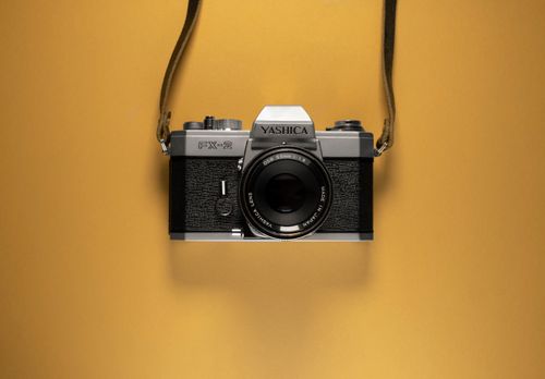 Free A classic Yashica FX-2 film camera suspended against a vibrant yellow backdrop, showcasing vintage appeal. Stock Photo
