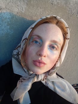 Close-up portrait of a young woman with heterochromia and headscarf in natural light. Artistic and vibrant makeup.