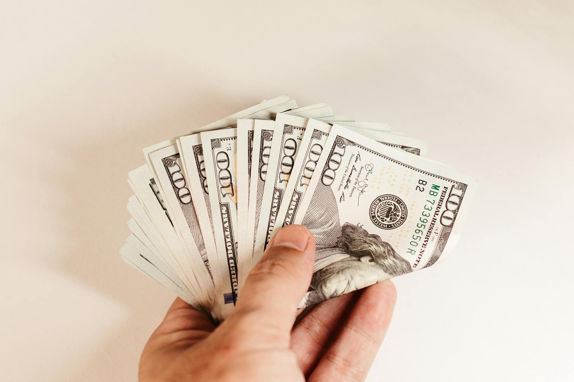 Close-up of a hand holding US hundred-dollar bills on a white background.