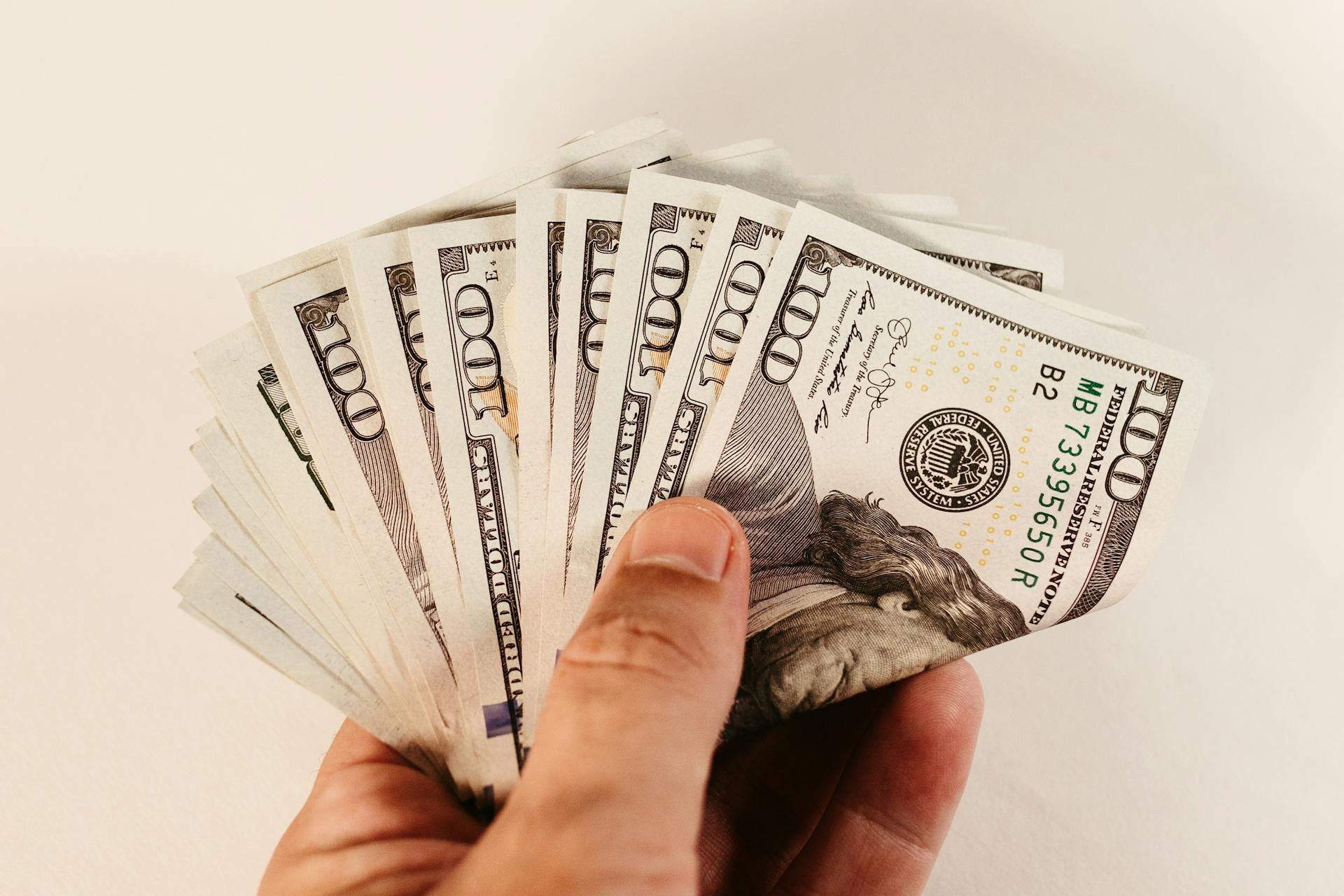 Close-up of a hand holding multiple US dollar bills against a white background.