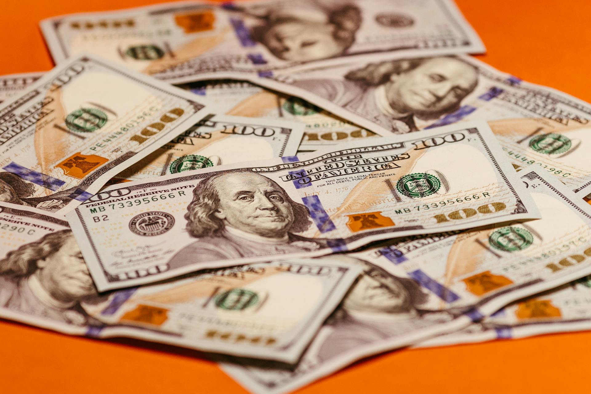 Scattered US $100 bills on a vibrant orange surface symbolizing wealth and finance.