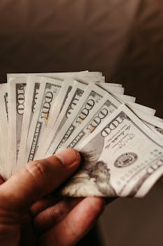Close-up of a hand holding several hundred dollar bills, representing wealth and finance.