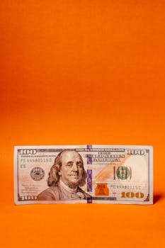 Crisp US hundred dollar bill displayed on a vibrant orange backdrop, highlighting financial themes.