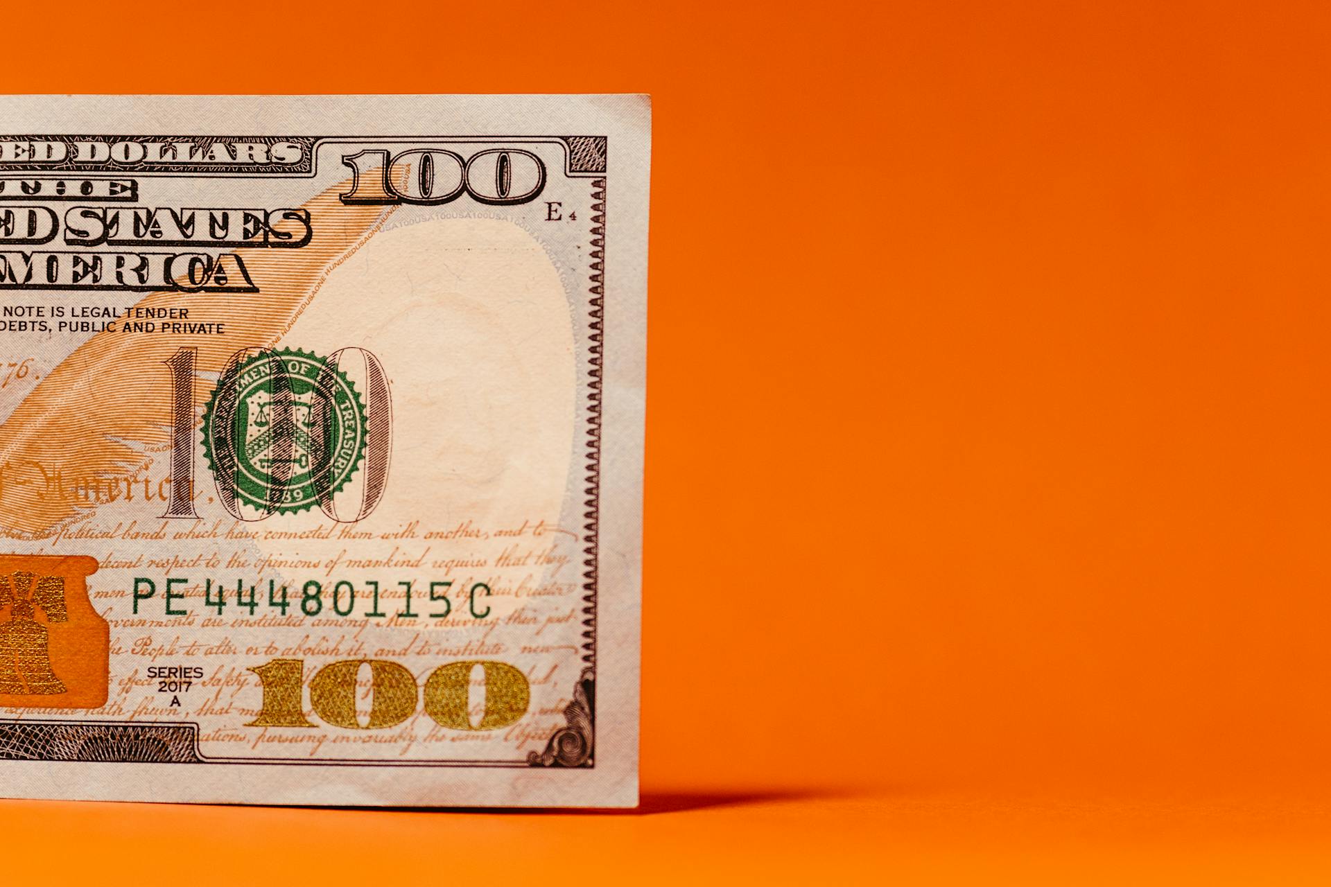 Detailed view of a US 100 dollar bill against a vibrant orange backdrop, highlighting currency concepts.