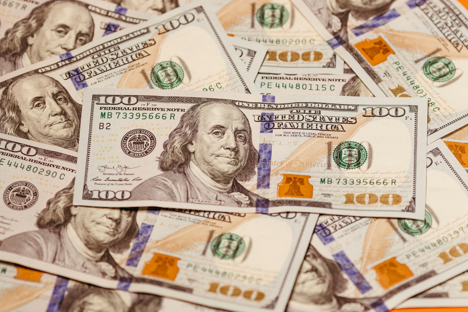 Close-up of multiple US hundred dollar bills featuring Benjamin Franklin, emphasizing wealth and finance.