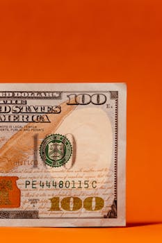 Close-up of a US hundred dollar bill with an orange background, showcasing financial themes.