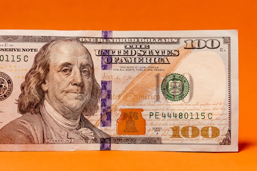 Detailed image of a US hundred dollar bill against a vibrant orange background.