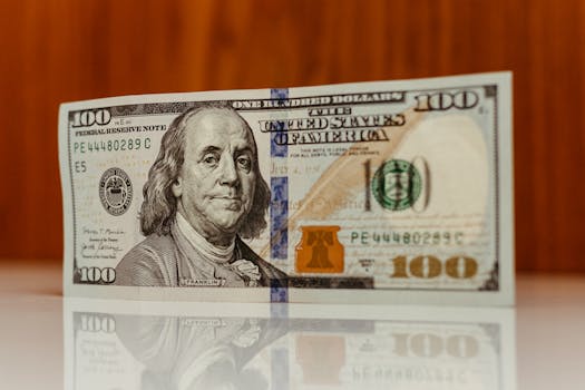 Crisp image of a $100 bill standing and reflecting on a smooth surface, highlighting details.