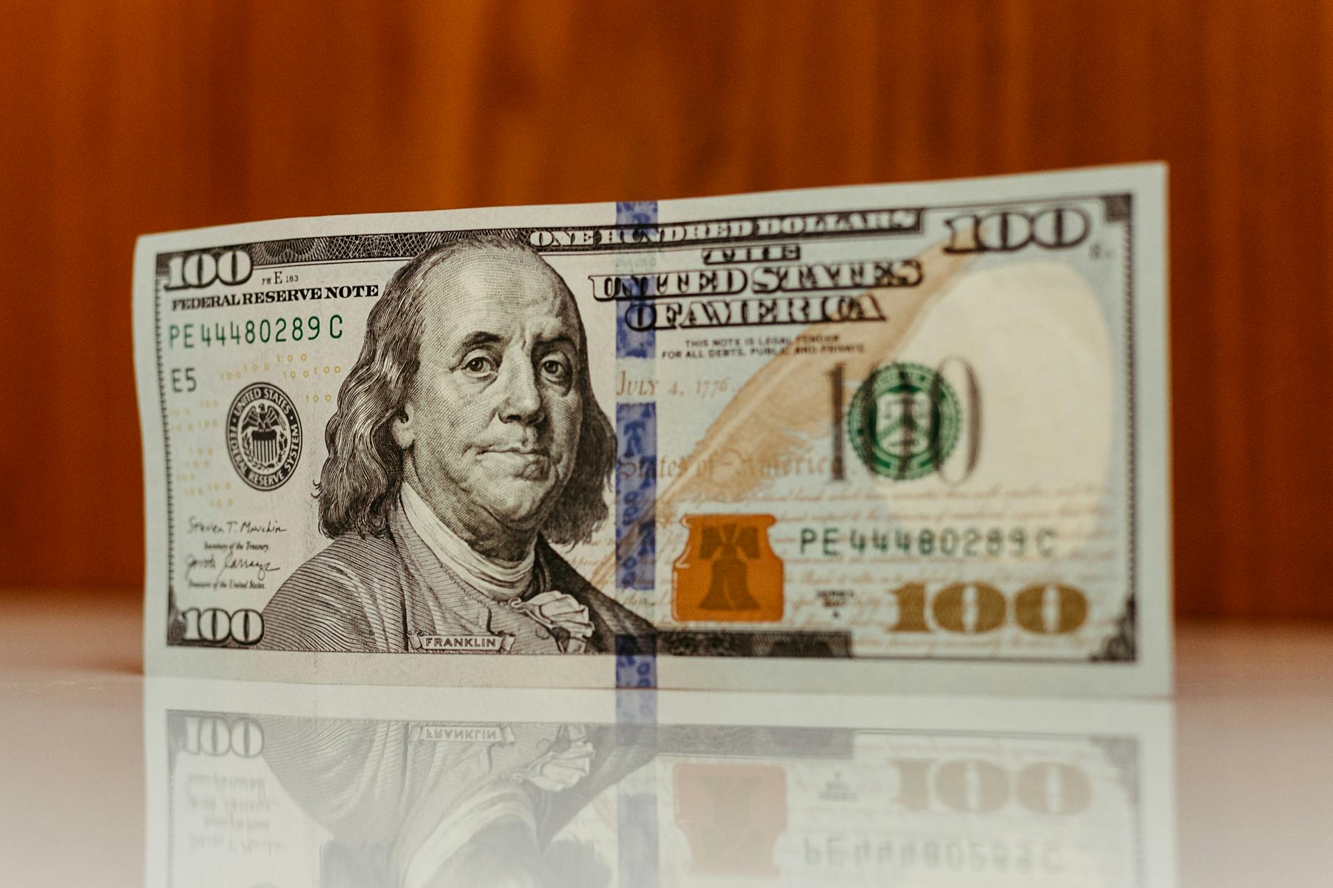 Crisp image of a $100 bill standing and reflecting on a smooth surface, highlighting details.