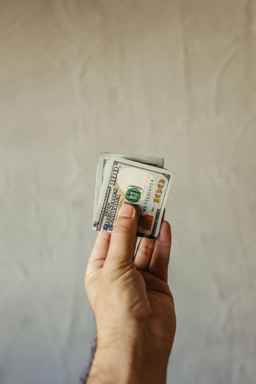 Free Close-up of a hand holding US dollar bills against a neutral background, symbolizing finance and economy. Stock Photo