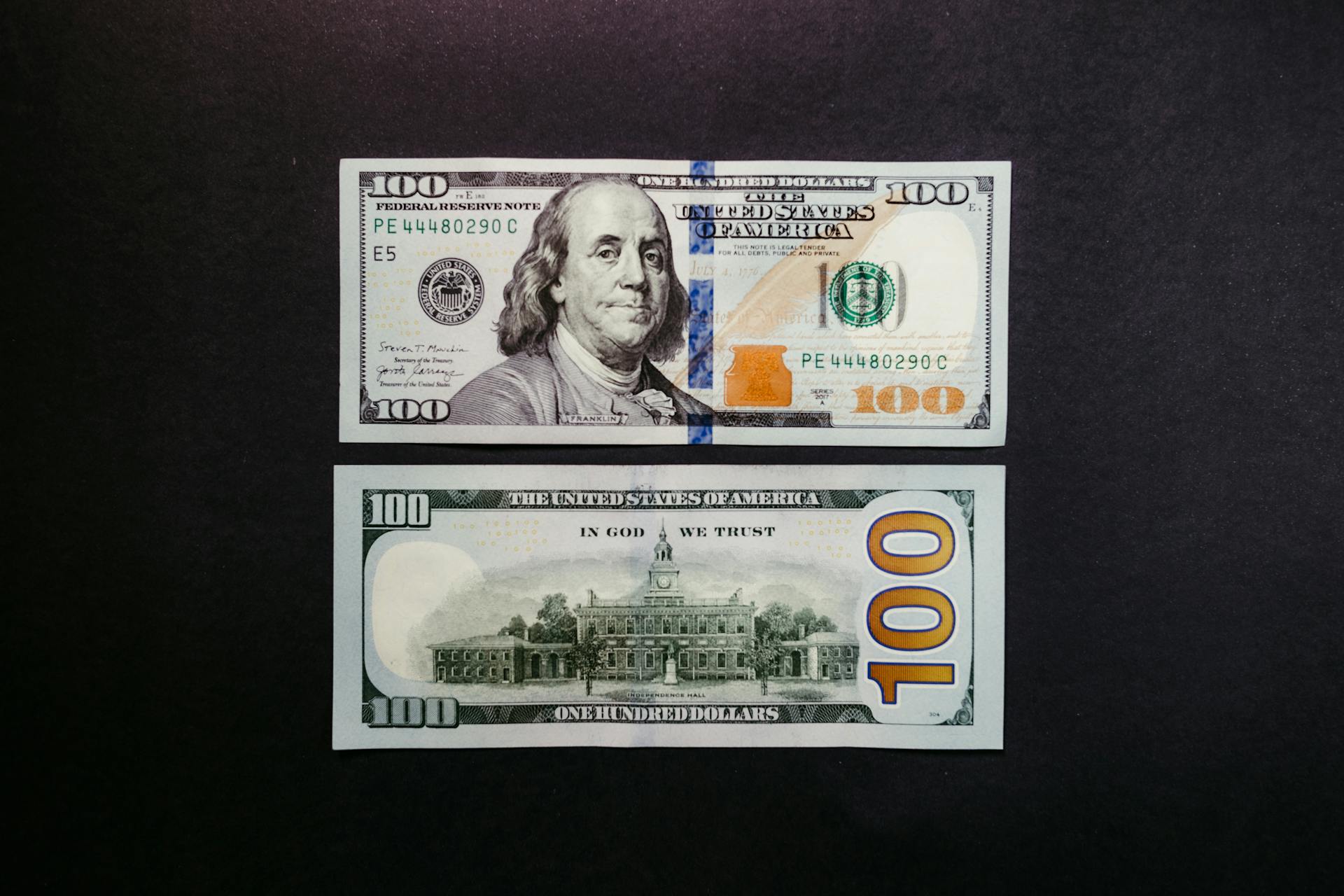 Detailed photo of US hundred dollar bills showing Benjamin Franklin and US currency design.