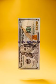 Crisp US hundred dollar bill against a vibrant yellow background, highlighting currency details.