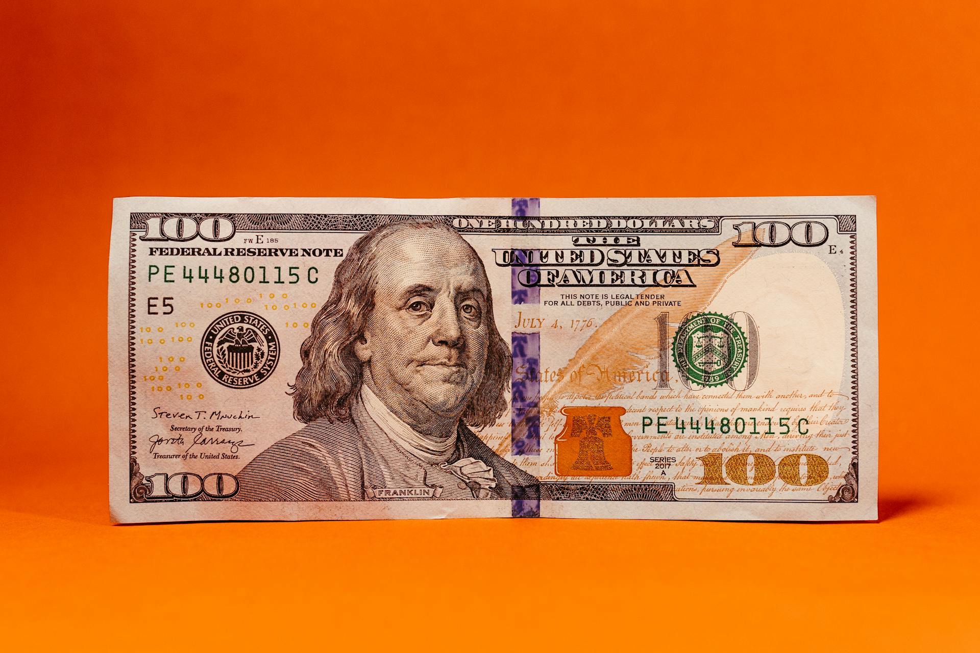 Detailed photo of a 100 dollar bill against a vibrant orange background, perfect for finance themes.