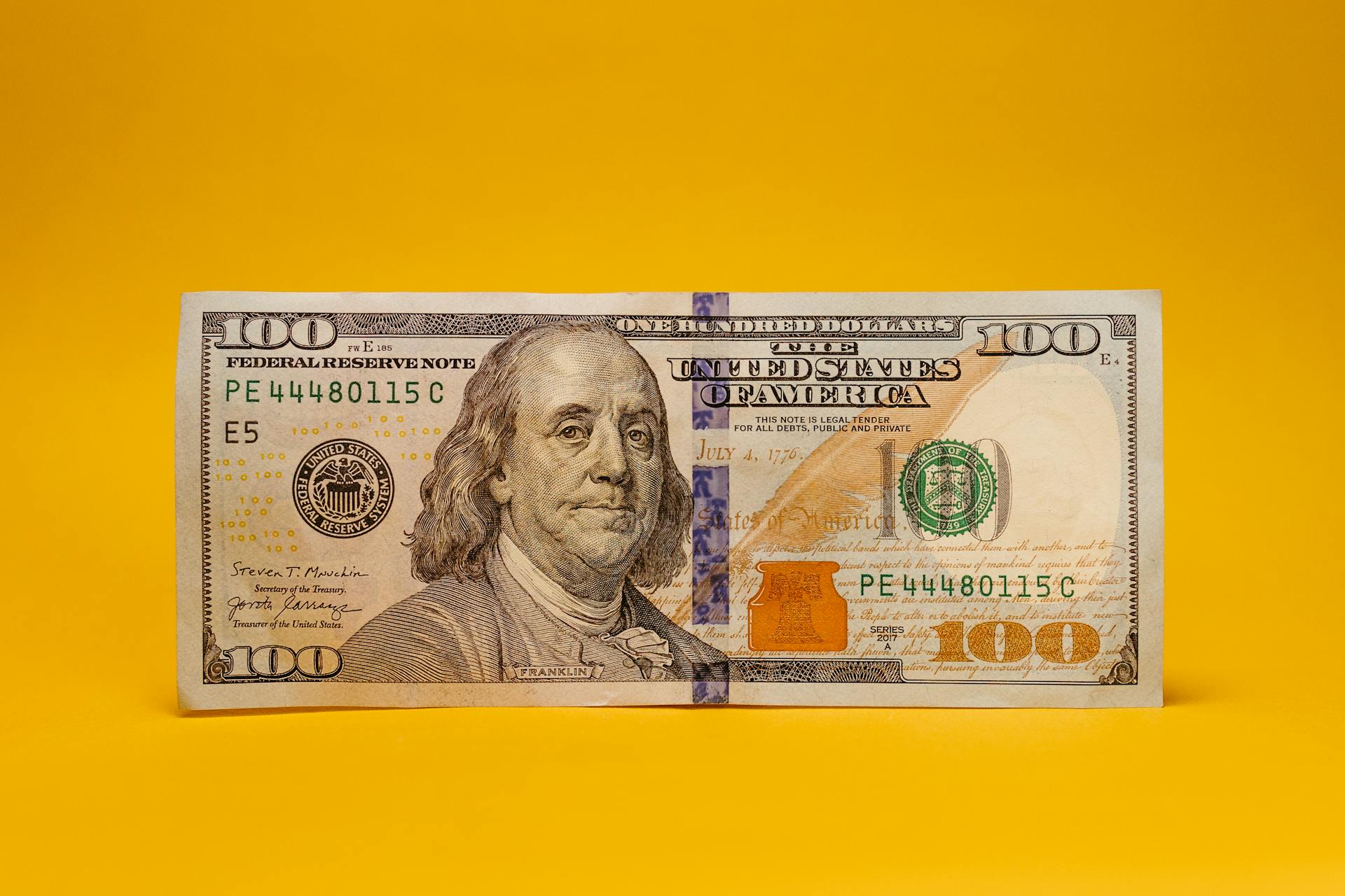 A close-up of a US hundred dollar bill on a warm yellow backdrop, ideal for financial themes.