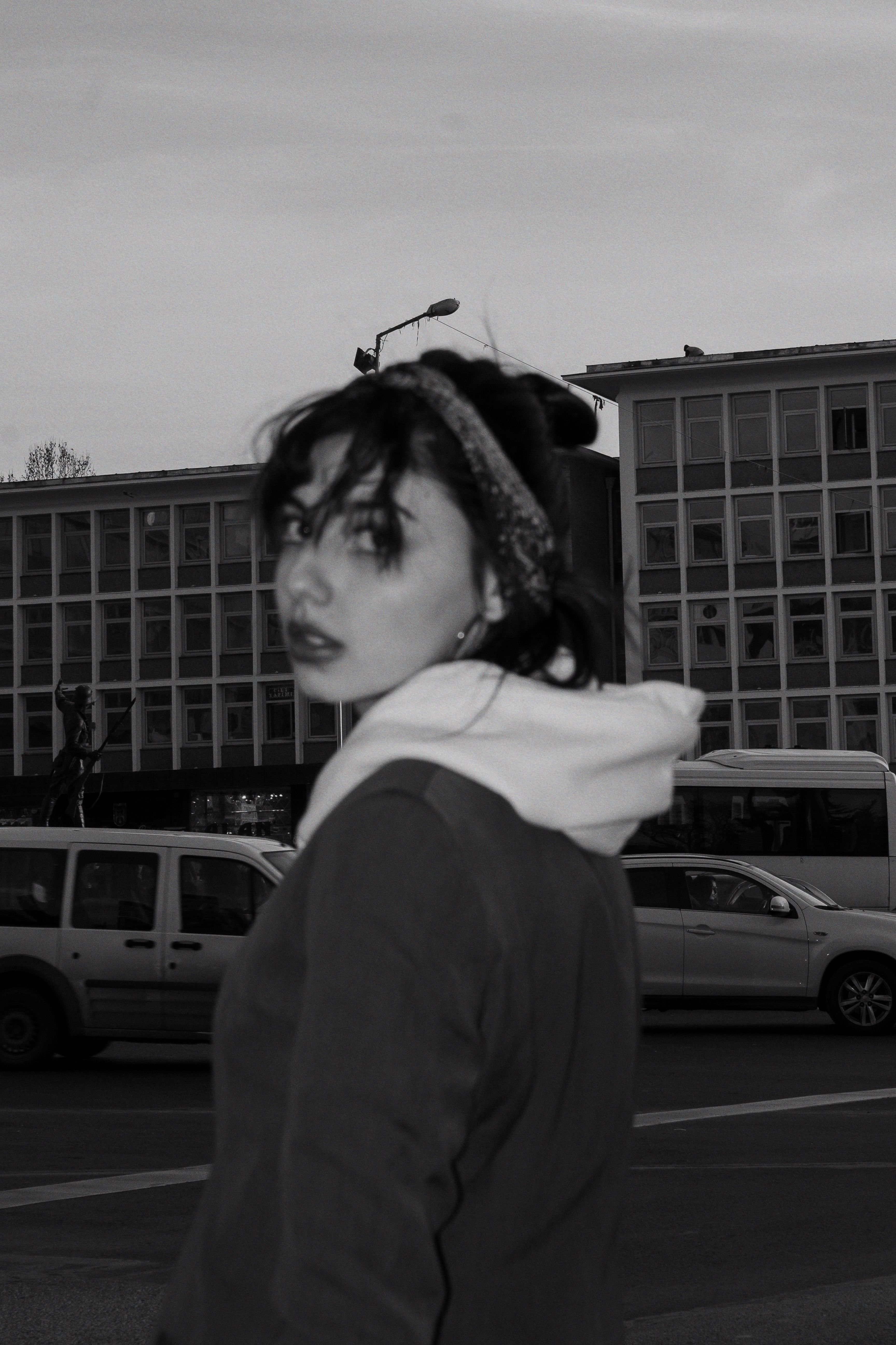 Black and white portrait of a woman in a hoodie in Ankara cityscape.