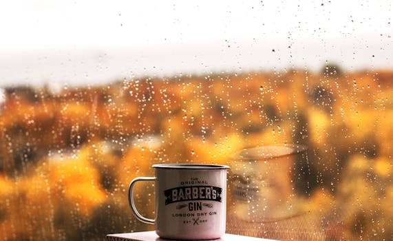 Metal coffee mug on windowsill with autumn view through raindrops.