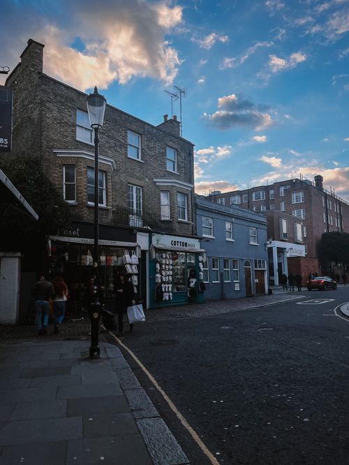 Free Picturesque urban street view with charming storefronts and pedestrians during dusk, showcasing a cozy city vibe. Stock Photo