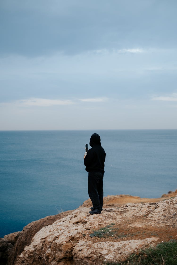 Person Standing On Rocky Ground Near A Body Of Water