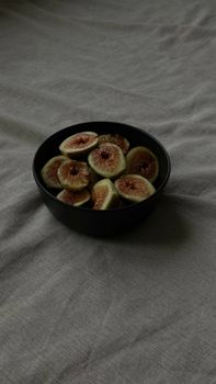 Vertical shot of sliced figs in a black bowl on a textured tablecloth, highlighting simple elegance.