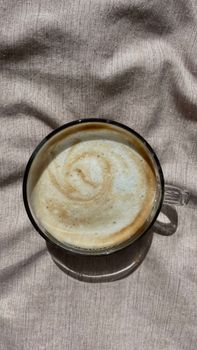 Top-down shot of a latte with a frothy swirl in a clear cup on a textured surface.