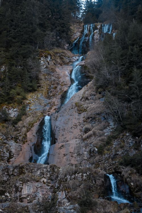 Free Beautiful flowing waterfall cascading down a rocky mountain amidst lush forest. Stock Photo